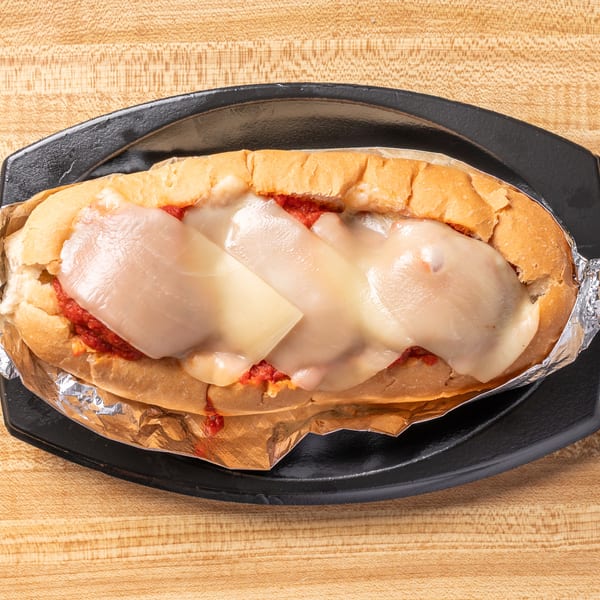 Meatball sub with melted cheese and red sauce, wrapped in foil on a black plate.