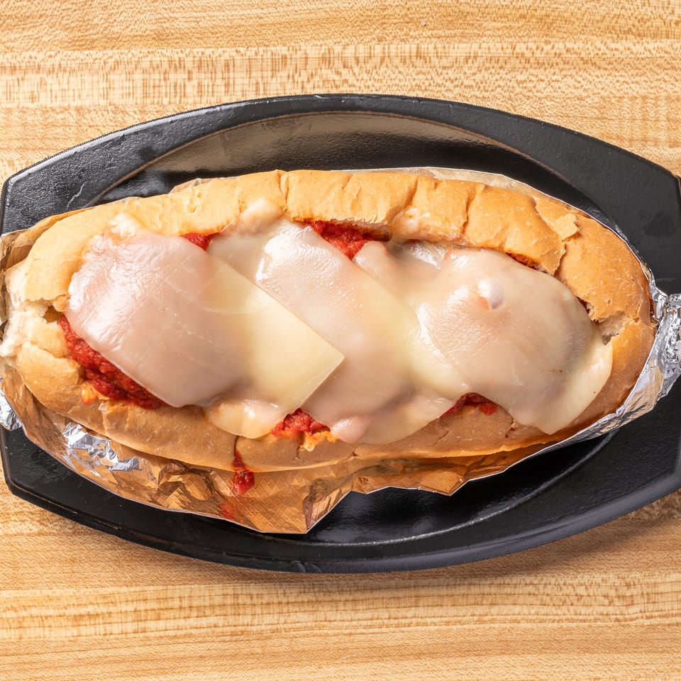 Meatball sub with melted cheese and red sauce, wrapped in foil on a black plate.