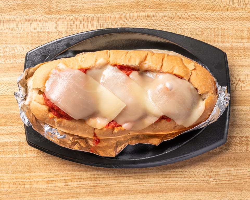 Meatball sub with melted cheese and red sauce, wrapped in foil on a black plate.