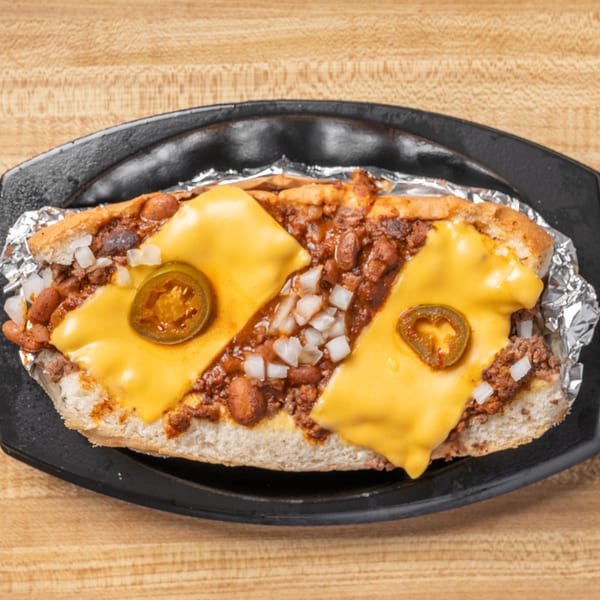Chili dog with melted cheese, diced onions, and jalapeño slices on a black plate.