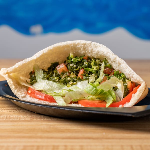 Pita bread stuffed with tabbouleh, lettuce, and sliced tomatoes on a black plate.