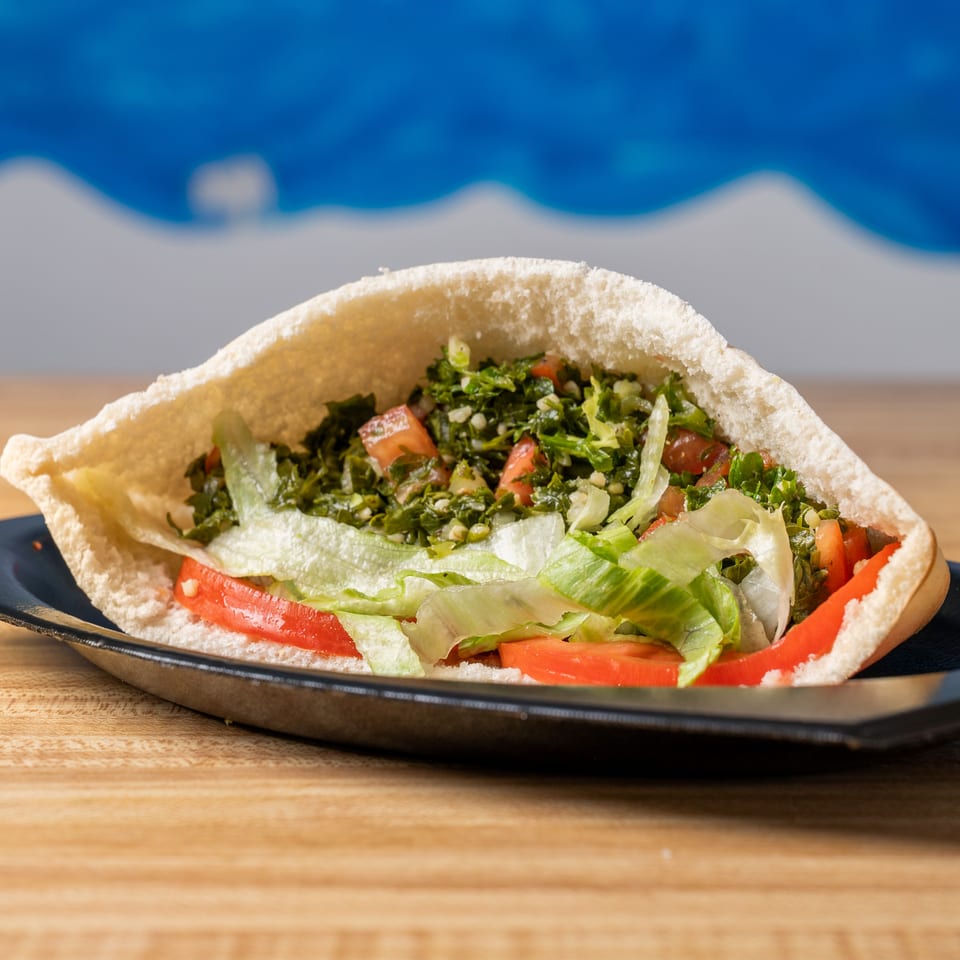 Pita bread stuffed with tabbouleh, lettuce, and sliced tomatoes on a black plate.