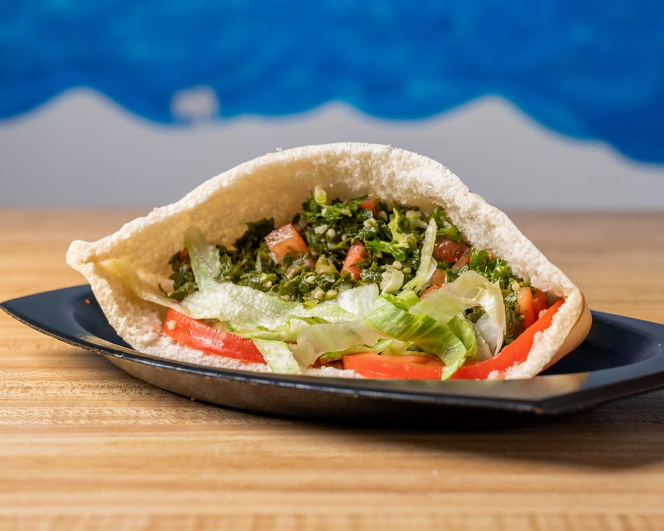 Pita bread stuffed with tabbouleh, lettuce, and sliced tomatoes on a black plate.