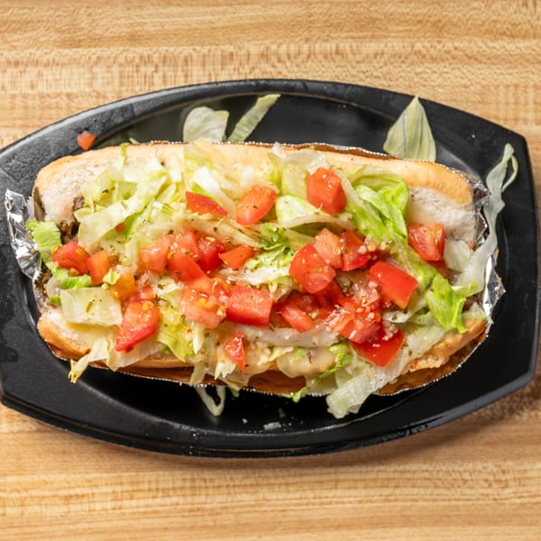 A long sub sandwich filled with lettuce and diced tomatoes, served on a black plate.