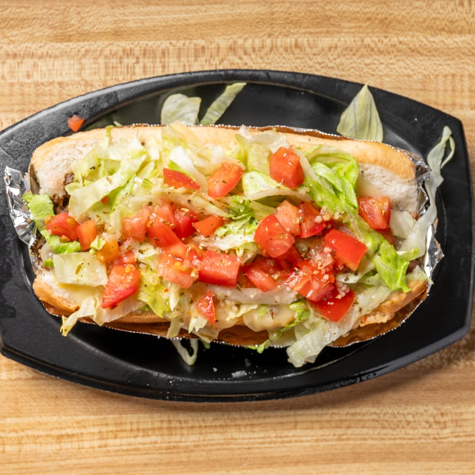 A long sub sandwich filled with lettuce and diced tomatoes, served on a black plate.