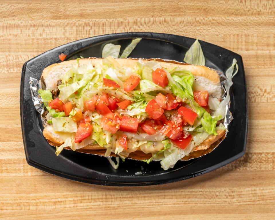 A long sub sandwich filled with lettuce and diced tomatoes, served on a black plate.