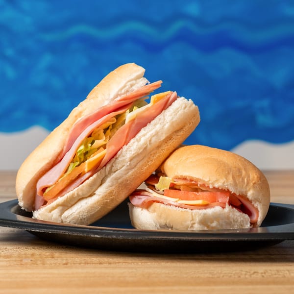 Two ham and cheese sandwiches, one sub and one round, on a black plate.