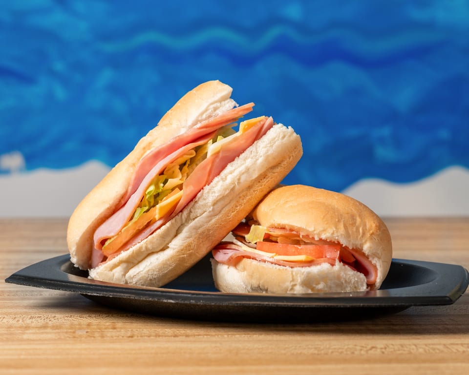 Two ham and cheese sandwiches, one sub and one round, on a black plate.
