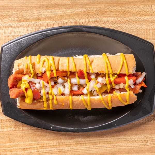 A hot dog with mustard, diced onions, and relish on a bun, served on a black plate.