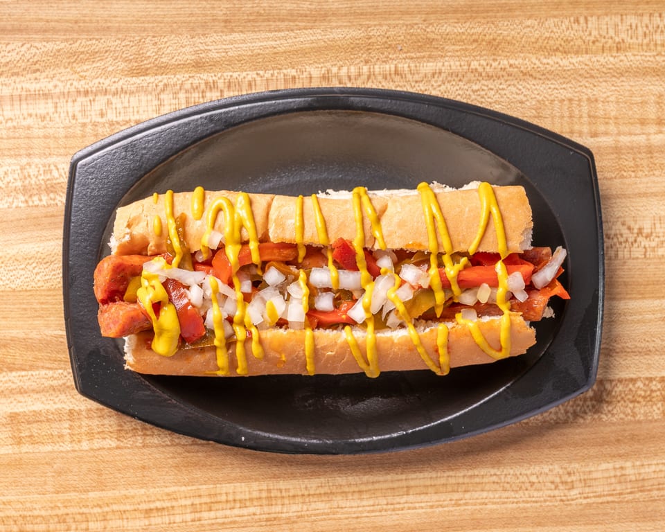 A hot dog with mustard, diced onions, and relish on a bun, served on a black plate.