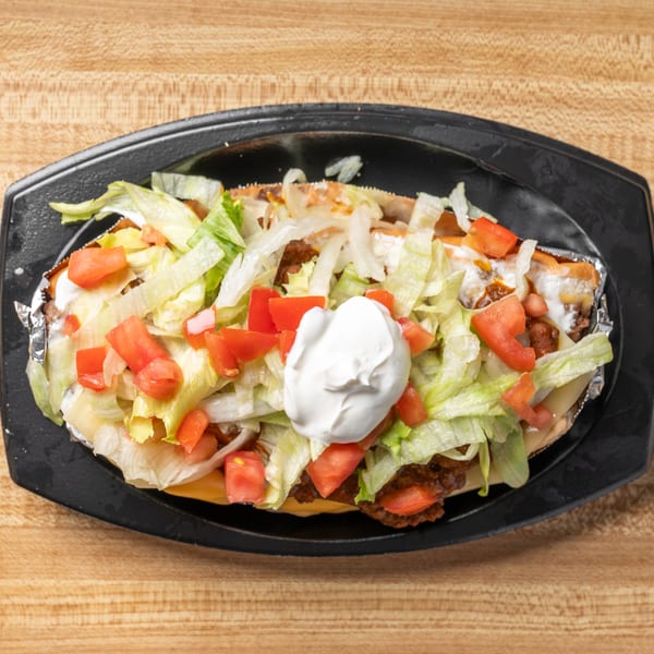Overhead view of a chili cheese dog with lettuce, tomatoes, and sour cream on a black plate.