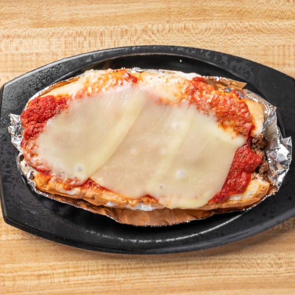 A meatball sub with melted cheese and red sauce, served in foil on a black plate.