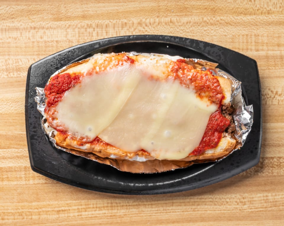 A meatball sub with melted cheese and red sauce, served in foil on a black plate.