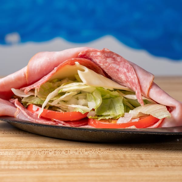 A large deli meat and cheese wrap with lettuce, tomatoes, and onions on a black plate.