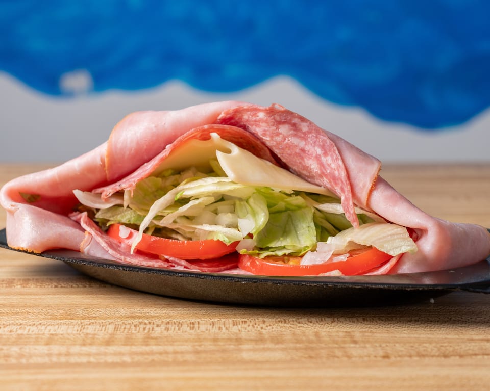 A large deli meat and cheese wrap with lettuce, tomatoes, and onions on a black plate.